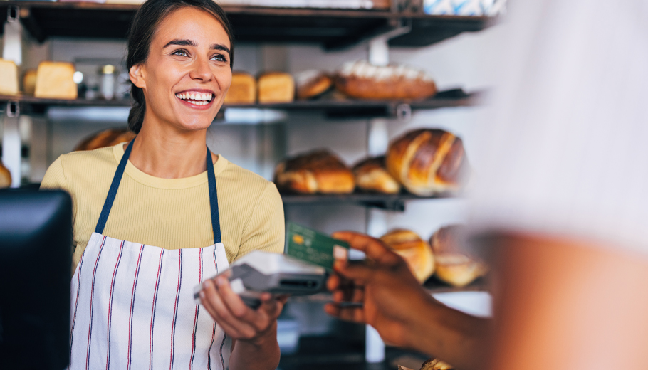 Person smiling at customer while holding a card reader while the customer makes pays for their items