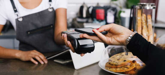 Barista holding a card reader to customer. Customer holding their phone near card reader to pay for food..